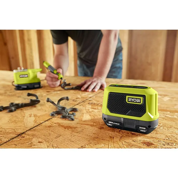 Ryobi ONE+ Akku-Bluetooth-Radio RBTM18-0 - 5 W, Ohne Akku - Nahaufnahme eines Ryobi ONE+ Bluetooth-Lautsprechers auf einer Holzoberfläche mit Werkzeugen im Hintergrund.