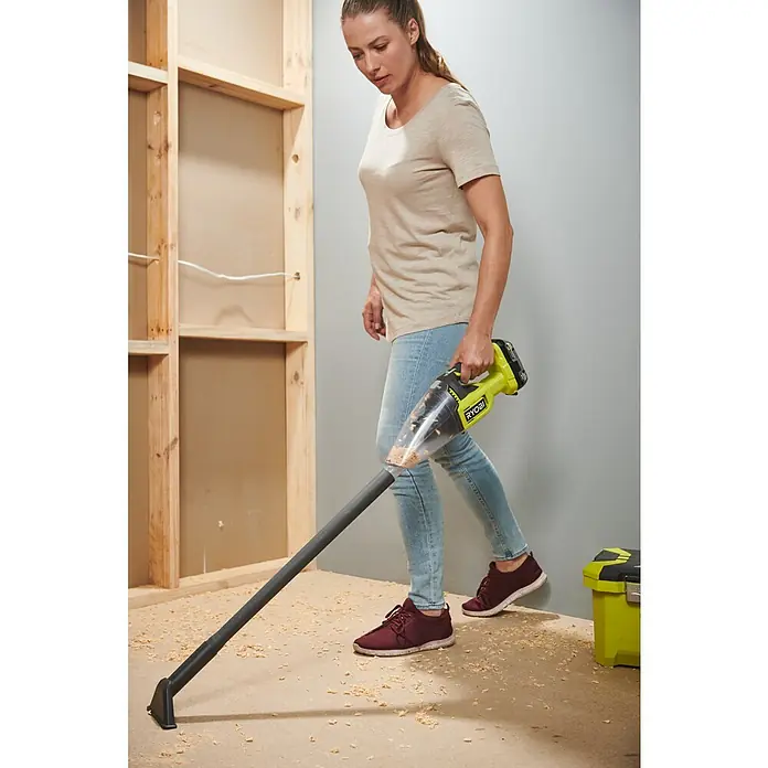 Ryobi ONE+ Akku-Staubsauger RHV18F-0 - 18 V, Ohne Akku, 600 ml - Eine Frau benutzt einen gelben Ryobi Akku-Handsauger mit einem langen Rohr, um Sägespäne von einem Boden zu entfernen.