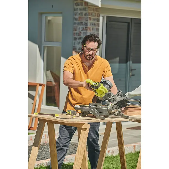 Ryobi ONE+ Akku-Kapp- & Gehrungssäge RMS18190-0 - 18 V, Ohne Akku, 3.600 U/min - Ein Mann benutzt eine RYOBI Kapp- und Gehrungssäge im Freien, um Holz zu schneiden, geschützt durch eine Schutzbrille.