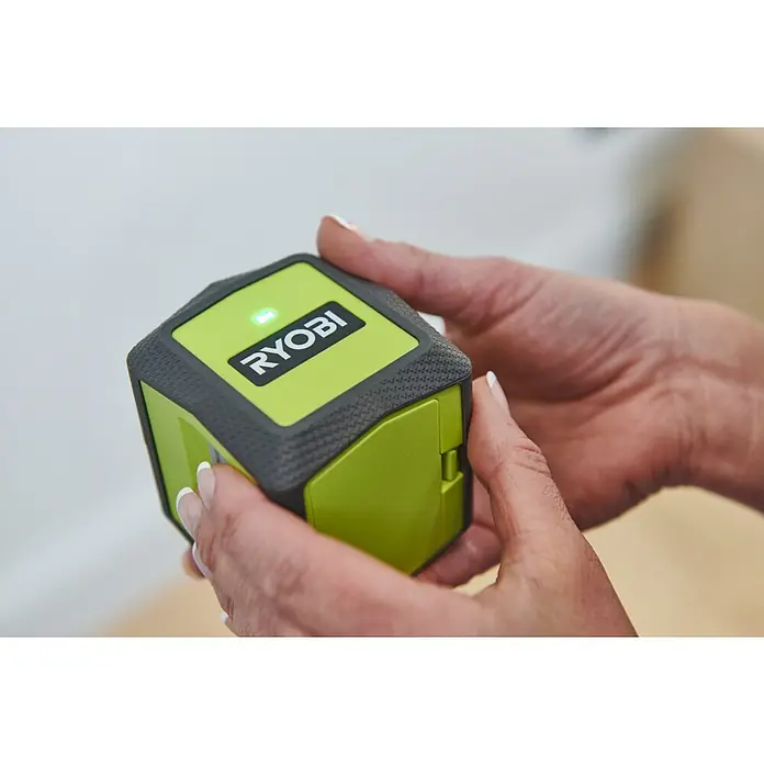 Ryobi Kreuzlinienlaser RBCLLG2 mit Skalamarkierung - Max. Arbeitsbereich: 15 m - Die Nahaufnahme einer Person, die einen grünen Ryobi-Würfellaser-Nivellierer in der Hand hält. Dieses Werkzeug ist kompakt und benutzerfreundlich.