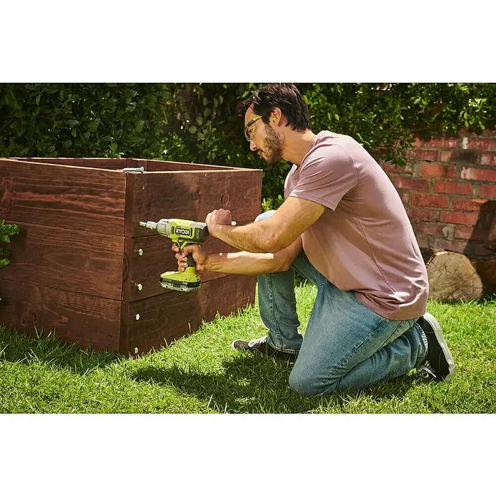 Ryobi ONE+ Akku-Schlagschrauber RIW18-0 - 18 V, Ohne Akku, 600 Nm - Ein Mann benutzt einen gelben RYOBI-Akkuschrauber, um eine hölzerne Pflanzkiste im Garten zusammenzubauen, um das Projekt abzuschließen.