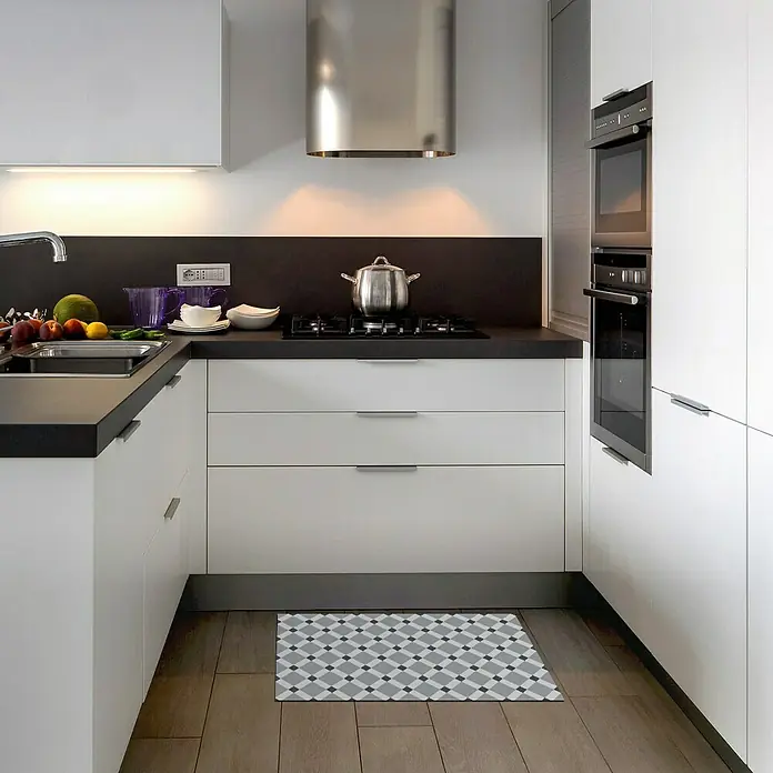 Alfombra de vinilo Croma BCN - Gris, 75 x 45 cm - Una alfombra rectangular con un patrón geométrico se coloca en una cocina moderna, complementando los armarios blancos y el suelo de madera.