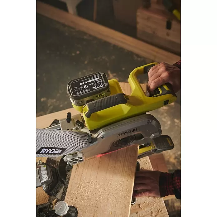 Ryobi ONE+ Akku-Kapp- & Gehrungssäge R18MS216-0 - 18 V, Li-Ionen, Ohne Akku, 0 U/min - 3.200 U/min - Gelb-graue Ryobi Akku-Kappsäge schneidet ein Holzbrett. Hände bedienen die Säge und halten das Holz.