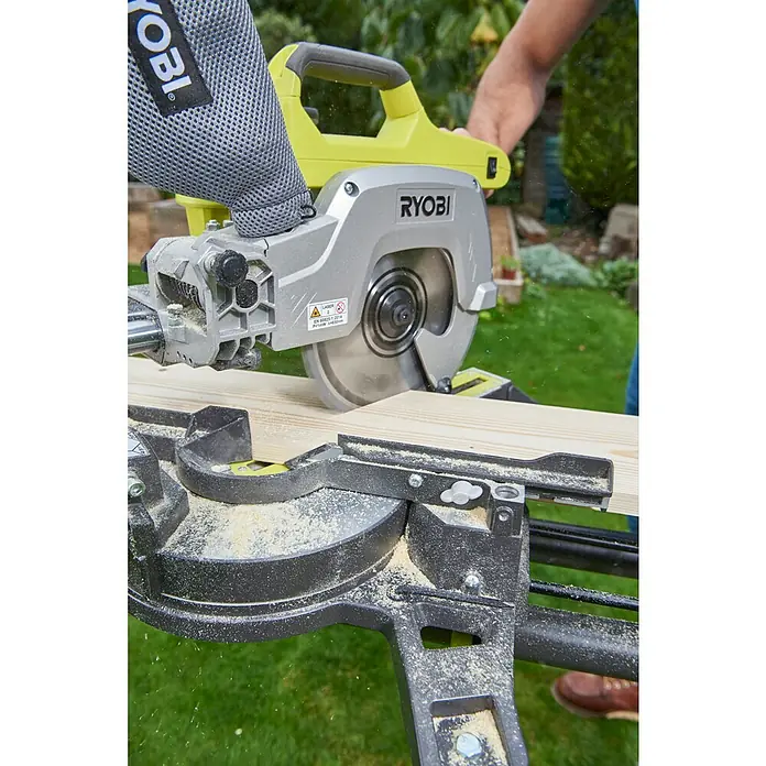 Ryobi ONE+ Akku-Kapp- & Gehrungssäge R18MS216-0 - 18 V, Li-Ionen, Ohne Akku, 0 U/min - 3.200 U/min - Nahaufnahme einer Ryobi-Gehrungssäge beim Schneiden eines Holzstücks im Freien, wobei der Fokus auf der Präzision und Funktionalität der Säge liegt.