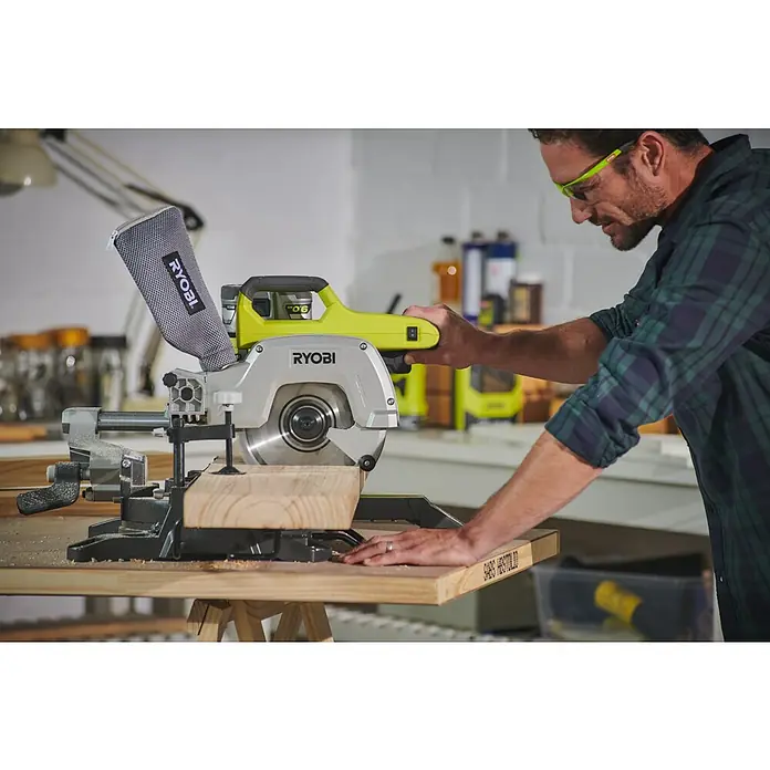 Ryobi ONE+ Akku-Kapp- & Gehrungssäge R18MS216-0 - 18 V, Li-Ionen, Ohne Akku, 0 U/min - 3.200 U/min - Eine Nahaufnahme einer RYOBI Kapp- und Gehrungssäge beim Sägen eines Holzstücks, mit einem Mann, der sie bedient.