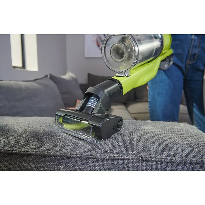 Ryobi Staubsaugeraufsatz RSVMBB - Passend für: Ryobi ONE+ Akku-Staubsauger RSV18-0, RSV18X und RSV18X1 - Nahaufnahme eines Ryobi-Staubsaugers, der Tierhaare von einem grauen Sofa entfernt, wobei der transparente Behälter Staub und Schmutz zeigt.