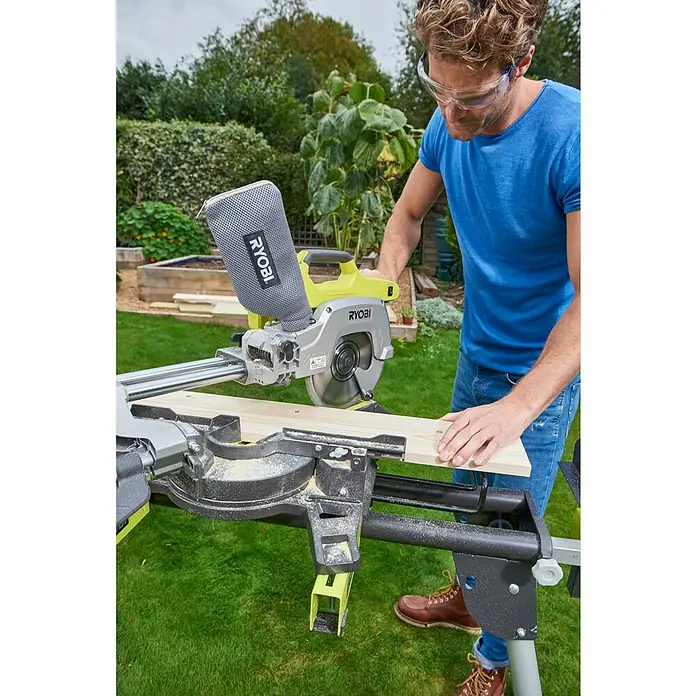 Ryobi ONE+ Akku-Kapp- & Gehrungssäge R18MS216-0 - 18 V, Li-Ionen, Ohne Akku, 0 U/min - 3.200 U/min - Ein Mann benutzt eine Ryobi Kapp- und Gehrungssäge mit Zugfunktion, um ein Stück Holz im Freien zu schneiden, und trägt dabei eine Schutzbrille.