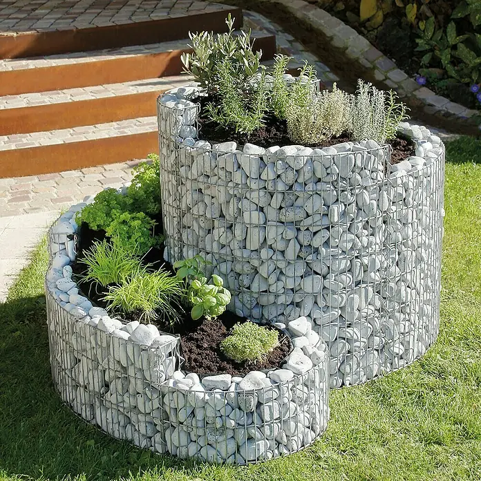 Bellissa Kräuterspirale - 140 x 110 x 80 cm - Der Gabionen-Pflanzenturm ist mit Kräutern bepflanzt und besteht aus Steinen und Drahtgitter. Er steht im Garten auf dem Rasen.