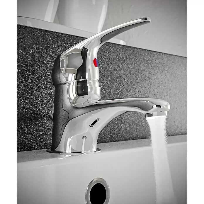 Mixomat Sirani Waschtischarmatur - Chrom, Glänzend - Glänzender Chrom-Wasserhahn mit rot/blauem Indikator, der Wasser in ein weißes Waschbecken spendet, vor einer dunklen strukturierten Wand.