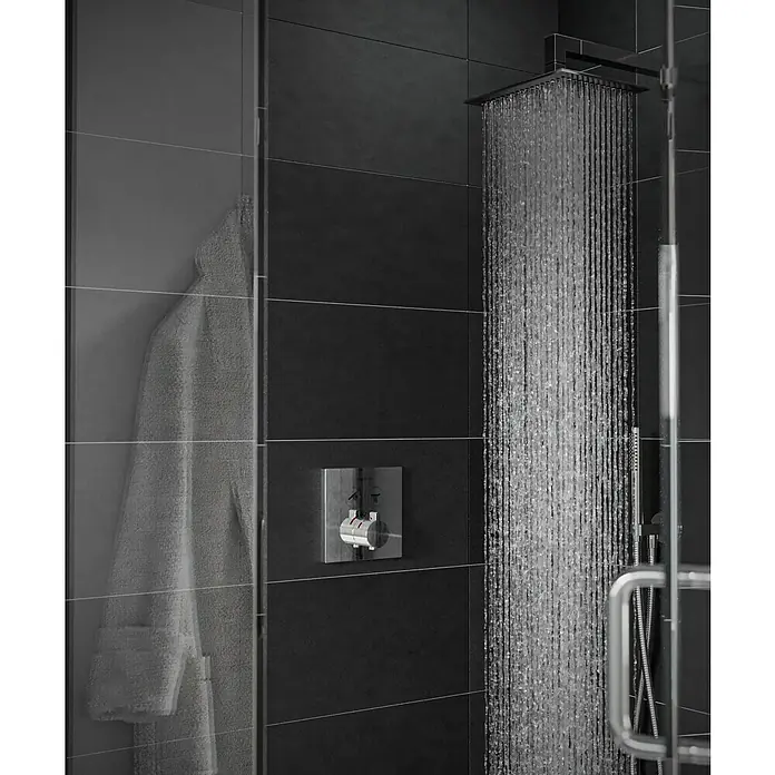 Hansgrohe UP-Thermostatarmatur ShowerSelect - Eckig, Chrom, Glänzend - Detailaufnahme einer modernen Dusche mit Regenduschkopf, dunklen Fliesen und einem weißen Bademantel im Hintergrund.