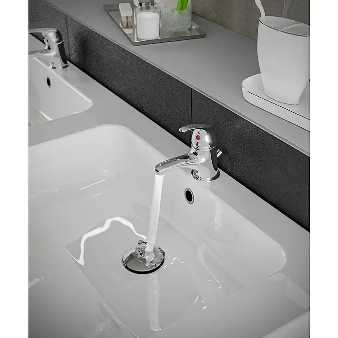 Mixomat Sirani WaschtischarmaturChrom, Glänzend - Ein Waschbecken mit einem modernen Chromwasserhahn, aus dem Wasser fließt, präsentiert die Sanitärkeramik in einem eleganten Badezimmerambiente.