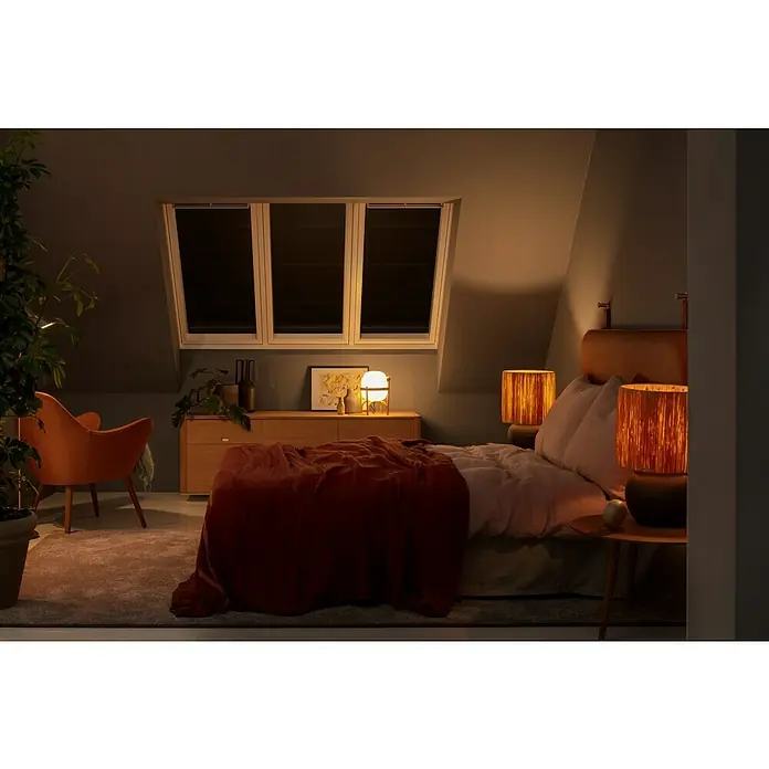 Velux Hitzeschutz-Markise Solar SSS - Passend für Fenstertyp: GGU, GGL, GPU, GPL, GHU, GHL, Passend für Fenstergröße: PK06, P06 - Ein gemütliches Schlafzimmer mit abgedunkelten Fenstern, beleuchtet von warmen Lampen, die eine entspannende Atmosphäre schaffen.