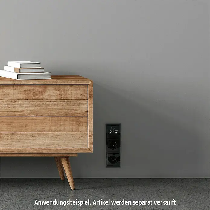 Busch-Jaeger Future Linear Abdeckrahmen 1723-181K - Anthrazit, 3-fach, Kunststoff - Eine Dreifach-Steckdose in Schwarz ist an einer grauen Wand montiert, neben einer Holzkommode mit Büchern.
