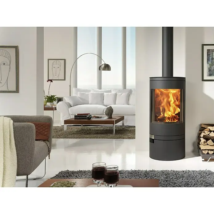 Panadero Kaminofen AKITA - 7,4 kW, Raumheizvermögen: 220 m³, Material Verkleidung: Stahl, Schwarz Metallic - Elegantes Wohnzimmer mit einem modernen Kaminofen, der Wärme und Stil vereint. Der Ofen ist ein Blickfang in dem hellen Raum.