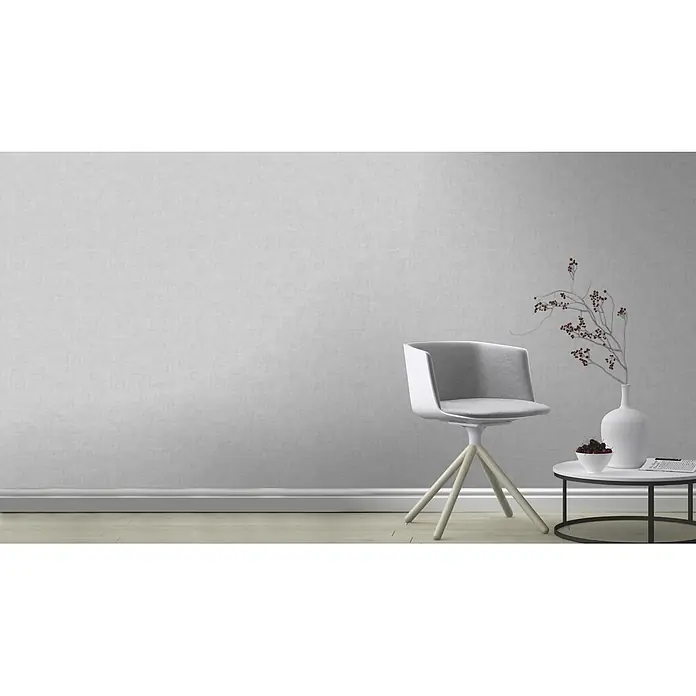 Rasch Vliestapete - Grau, Uni, 10,05 x 0,53 m, Schimmernd - Ein moderner Stuhl mit einem weißen Gestell und einem grauen Sitzbereich, der neben einem kleinen Tisch mit Dekoration steht.