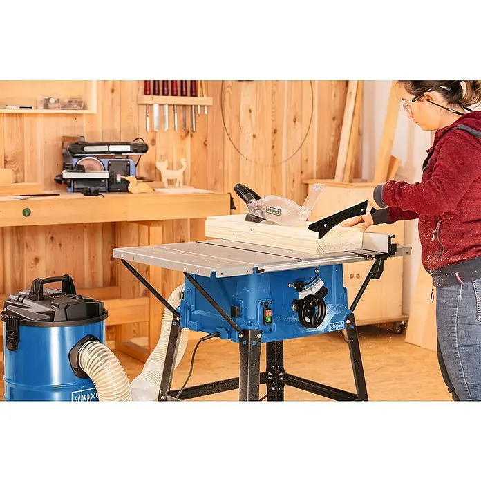 Scheppach Tischkreissäge HS100S - 2.000 W, Durchmesser Sägeblatt: 250 mm, Schnitttiefe bei 90 °: 85 mm - Eine Frau bedient eine Scheppach Tischkreissäge in einer Werkstatt, inklusive Staubsauger zur Säuberung des Arbeitsplatzes.