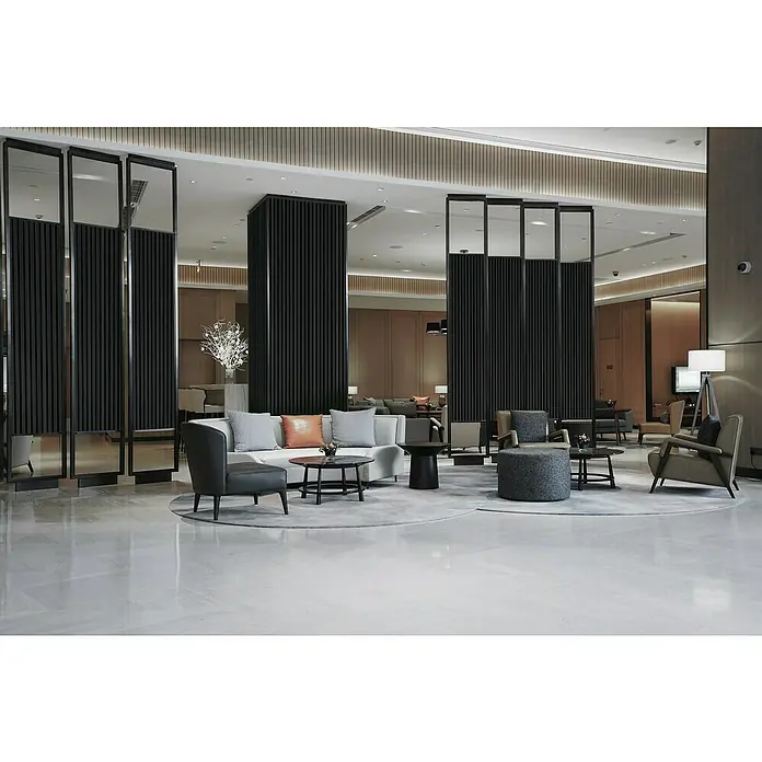 FibroTech Akustikpaneel Proff - Schwarz, Eiche, 3.000 x 605 x 22 mm - Einladende Lobby mit stilvollen Sitzmöbeln, getrennt durch elegante Raumteiler. Helle, polierte Böden und modernes Design.