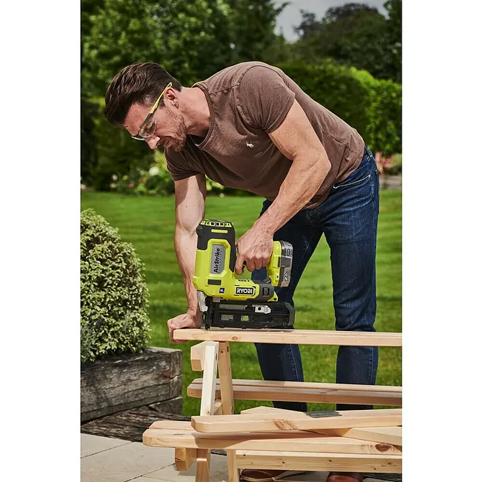 Ryobi ONE+ Akku-Nagler R16GN18-0 - 18 V, Ohne Akku, Länge Nagel: 19 mm - 64 mm - Ein Mann benutzt einen Ryobi AirStrike Nagler, um Holz zu bearbeiten. Der Nagler ist gelb-schwarz und scheint kabellos zu sein.