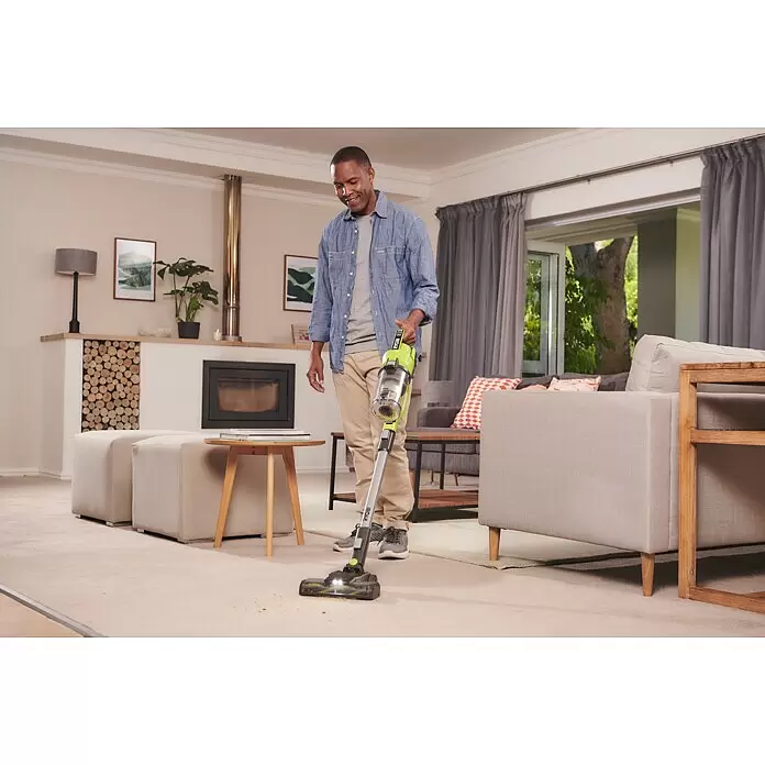 Ryobi ONE+ Maschinenpaket - Akku-Staubsauger RSV18-0 + gratis Starter-Kit - Grün-grauer Akku-Stielstaubsauger, von einem Mann zum Teppichsaugen verwendet.