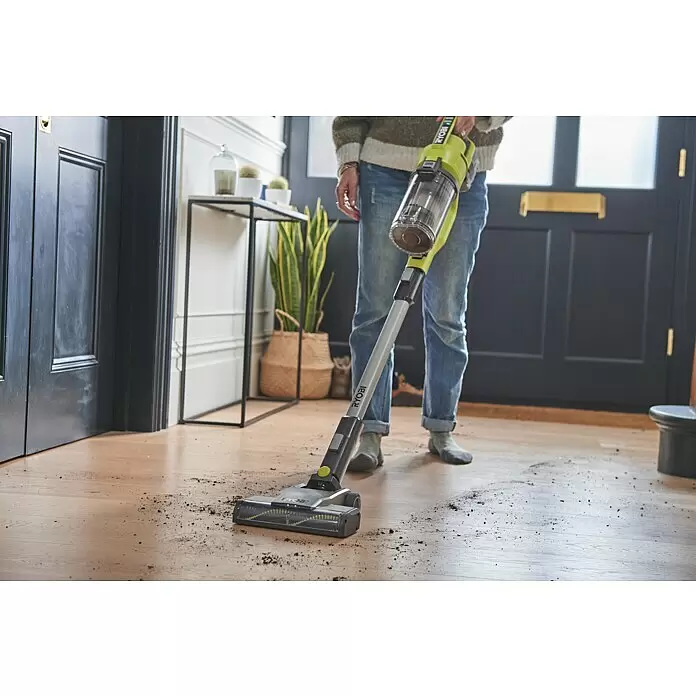 Ryobi ONE+ Maschinenpaket - Akku-Staubsauger RSV18-0 + gratis Starter-Kit - Person reinigt schmutzigen Holzfußboden mit grün-grauem Akku-Stielstaubsauger.