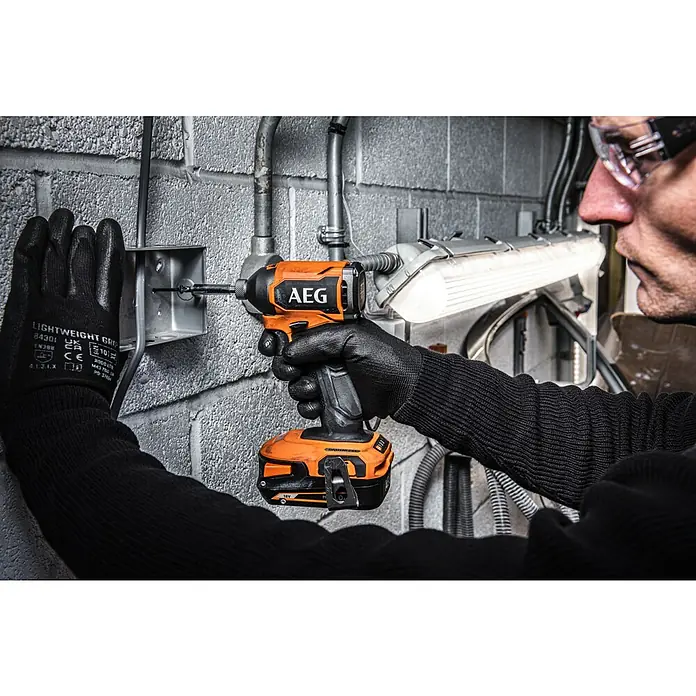 AEG Pro 18V Akku-Schlagschrauber BSS18SBL2-0 - 18 V, Ohne Akku, 200 Nm - Ein Handwerker befestigt eine Metallbox mit einem AEG Akku-Schlagschrauber an einer Ziegelwand. Der orange-schwarze Schrauber ist im Fokus.