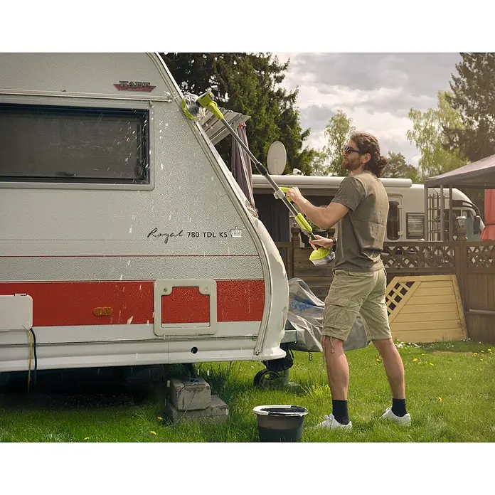 Ryobi ONE+ Akku-Reinigungsbürste R18TPS-0 - 18 V, Ohne Akku - Mann reinigt einen Wohnwagen mit einem gelben Hochdruckreiniger. Der Wohnwagen steht auf einem grünen Rasen neben einem Eimer.
