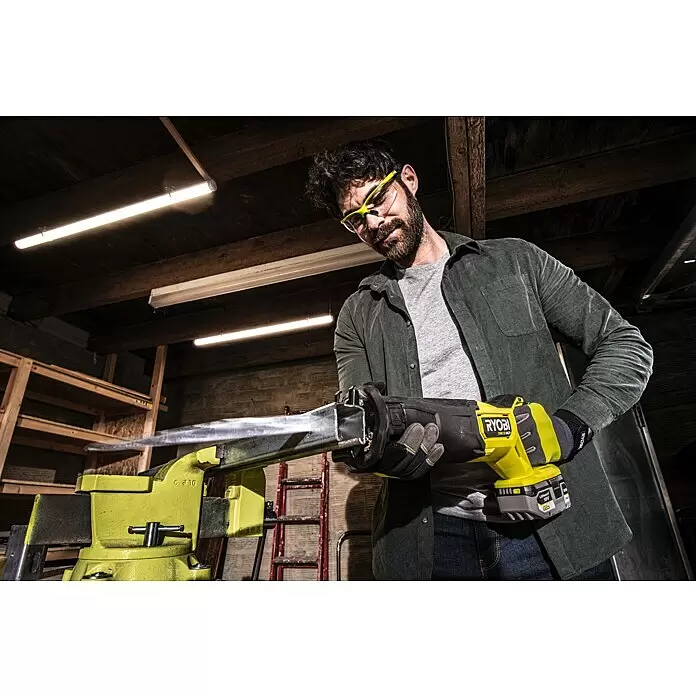 Ryobi ONE+HP Akku-Säbelsäge RRS18X-0 - 18 V, Hublänge: 32 mm, Ohne Akku - Mann mit Schutzbrille und Handschuhen benutzt eine gelb-schwarze Ryobi 18V Akku-Säbelsäge, um einen Metallstab in einem hellgrünen Schraubstock zu schneiden.