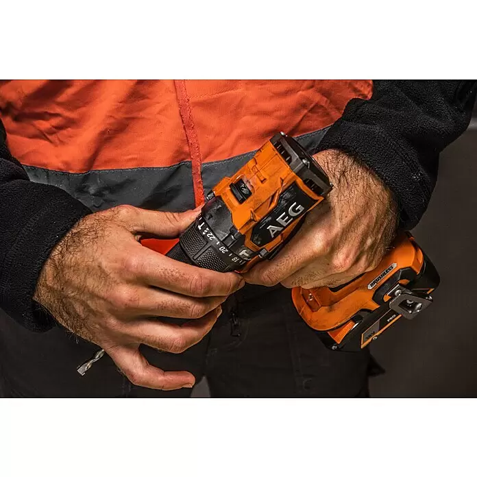 AEG Pro 18V Taladro atornillador de batería BS18SBL-202C - 18 V, 2 baterías, 2 Ah, 60 Nm - Primer plano de una persona sosteniendo un taladro inalámbrico AEG naranja y negro, con una broca visible.