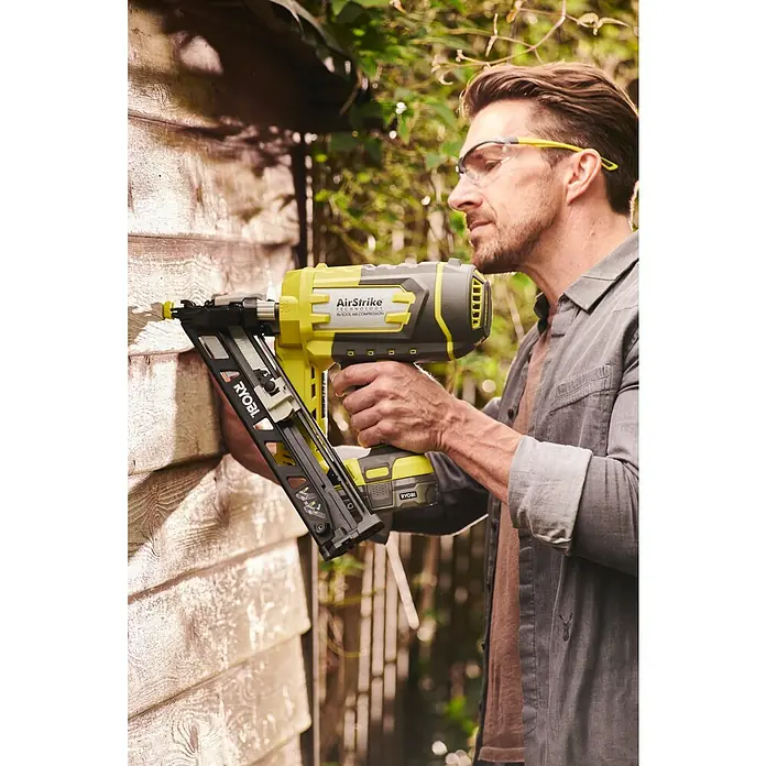 Ryobi ONE+ Akku-Nagler R15GN18-0 - 18 V, Ohne Akku - Ein Mann benutzt einen gelben Ryobi AirStrike Akku-Nagler zum Bauen, mit Schutzbrille.