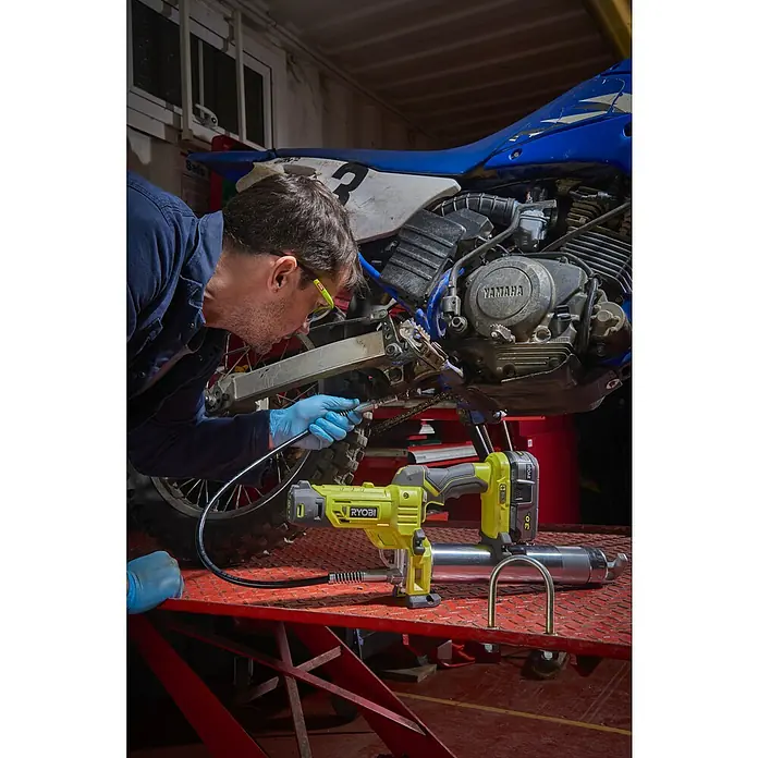 Ryobi ONE+ Akku-Fettpresse R18GG-0 - 18 V, Ohne Akku, Li-Ionen, Max. Druck: 690 bar - Ein Mann wartet ein Motorrad mit einer Ryobi-Fettpresse. Das Werkzeug steht auf einem roten Tisch, während er das Motorrad schmiert.
