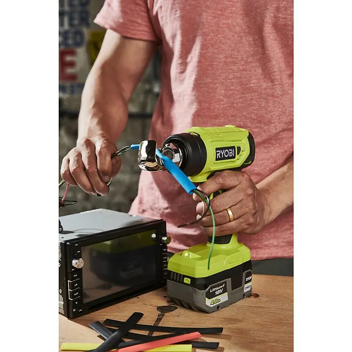 Ryobi ONE+ Akku-Heißluftgebläse R18HG-0 - 0 °C - 470 °C, Ohne Akku - Ein Mann benutzt eine RYOBI Heißluftpistole, um Schrumpfschläuche auf Kabeln anzubringen, die mit einem Autoradio verbunden sind.