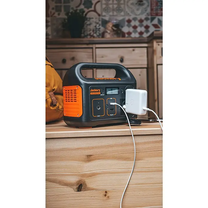 Jackery Estación de energía portátil Explorer 240 Pro EU - 240 Wh, Negro, 16,8 Ah - La estación de energía Jackery Explorer 240, una fuente de energía portátil, se carga con un cargador blanco en una superficie de madera.