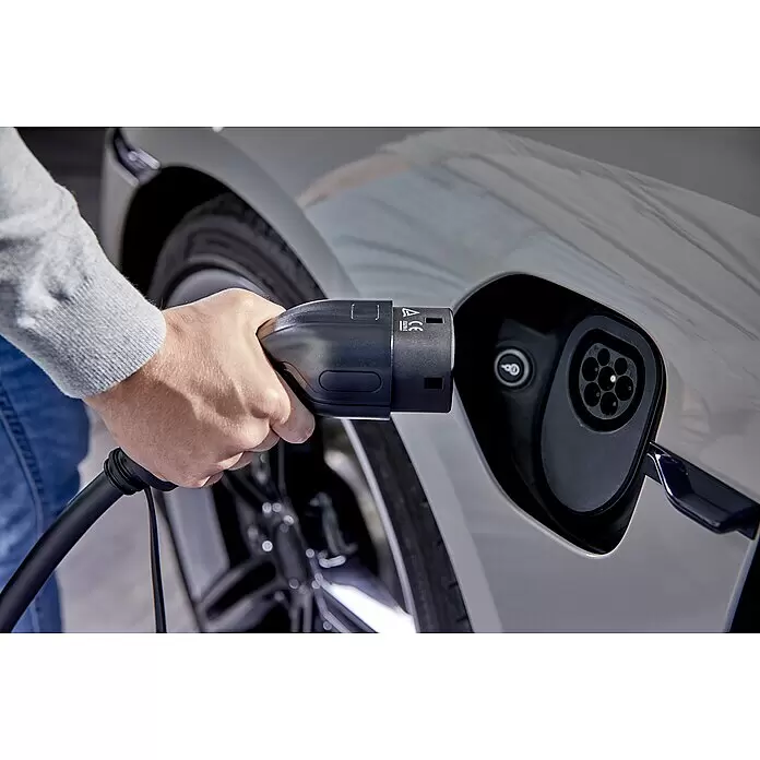 AEG Kfz-Ladekabel Schuko-Stecker zu Typ 2 Stecker - Kabellänge: 7 m - Hand steckt schwarzen Elektrofahrzeug-Ladestecker in den Ladeanschluss eines hellen Autos.