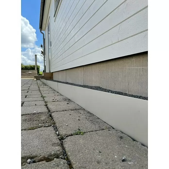 Recal Rasenkante Recal - 1.100 x 1,6 x 100 mm, Silber, Metall - Weiße Randbegrenzung trennt graue Pflastersteine von einem Kiesbett entlang einer Hauswand.