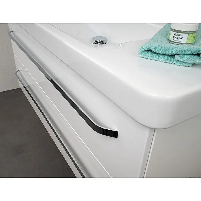 Lanzet K2 Waschtischunterschrank117,9 x 45,3 x 48,9 cm, Weiß - Nahaufnahme eines weißen Waschbeckens mit Handtuch und Hautpflegeprodukt, das ein elegantes und modernes Badezimmerdesign präsentiert.