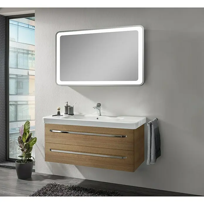Lanzet K2 Waschtischunterschrank - 117,9 x 45,3 x 48,9 cm, Berg Eiche - Ein moderner Waschtisch mit zwei Schubladen und einem beleuchteten Spiegel hängt an der Wand und sorgt für eine elegante Badezimmeratmosphäre.