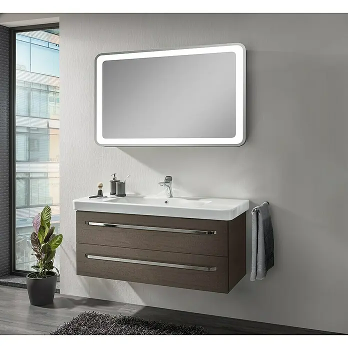 Lanzet K2 Waschtischunterschrank - 117,9 x 45,3 x 48,9 cm, Eiche Maron - Das Bild zeigt ein modernes Badezimmer mit einem beleuchteten Spiegel über einem Waschtisch mit Schubladen und einem Handtuchhalter.
