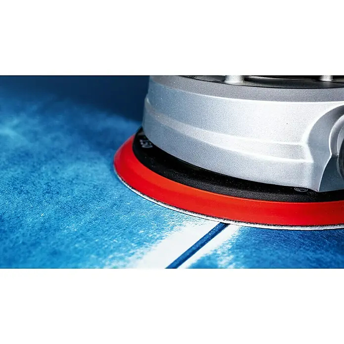 Bosch Expert Haftschleifscheiben-Set C470Durchmesser: 225 mm, 6 Stk. - Nahaufnahme eines silbernen Exzenterschleifers mit rotem Rand, der auf einer blau-weißen Oberfläche arbeitet.
