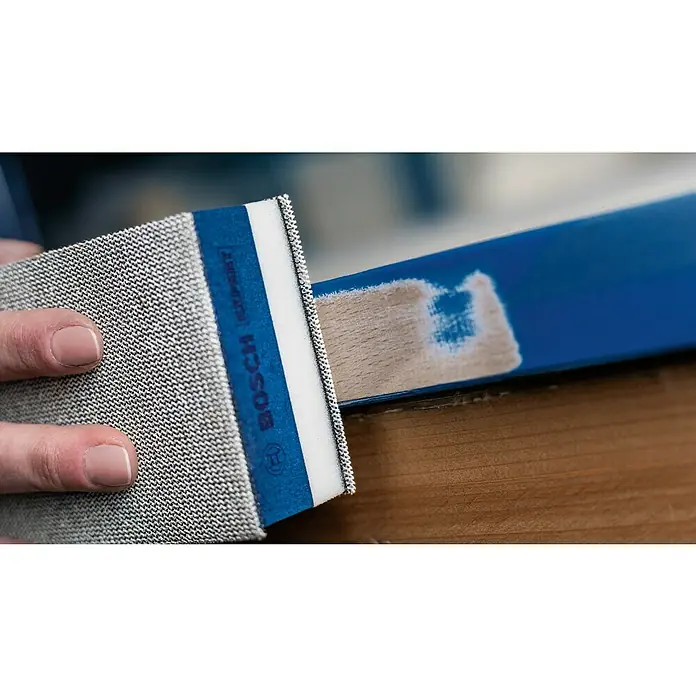 Bosch Expert Schleifblock Dual Density Set M480 - Maße Handschleifer: 80 x 133 mm - Nahaufnahme eines Bosch Schleifpads, das Farbe von einem blauen Holzstück entfernt, um die Holzoberfläche freizulegen.