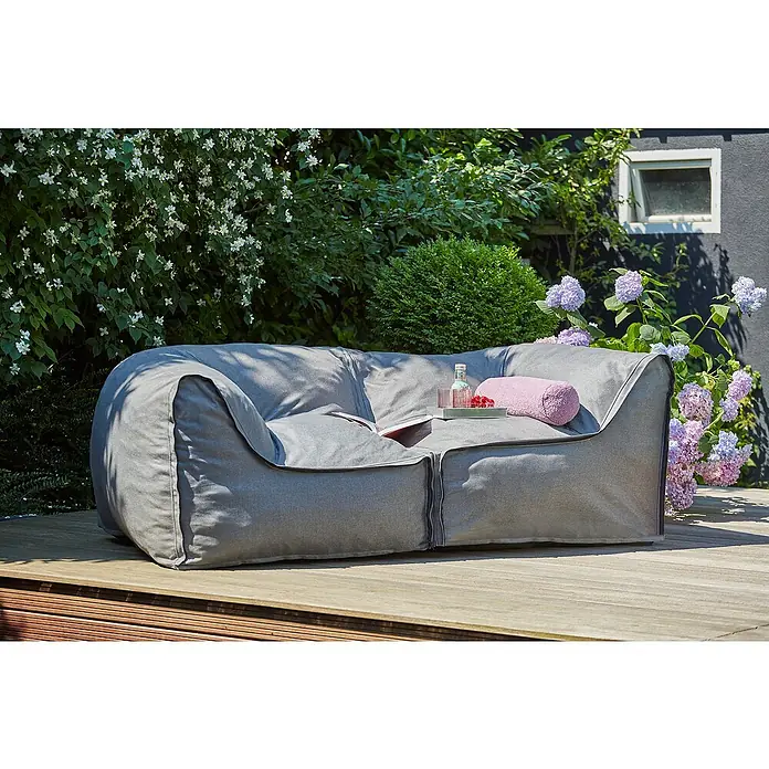 Loungemöbel-Set modular - 2 -tlg., Olefin, 2 Ecken, Grau - Ein graues Outdoor-Sofa aus Stoff mit Kissen und Getränken auf einer Holzterrasse, umgeben von üppigem Grün und Blumen.