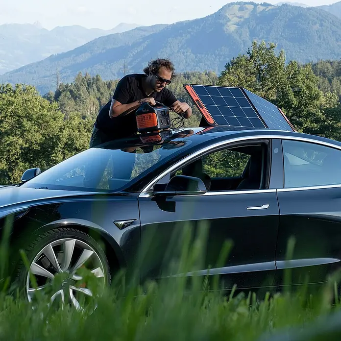 Jackery Estación de energía portátil Explorer 500 Pro EU - 500 Wh, Negro, 24 Ah - Un hombre conecta una estación de energía Jackery a un panel solar en el techo de un Tesla negro. Energía ecológica en la naturaleza.