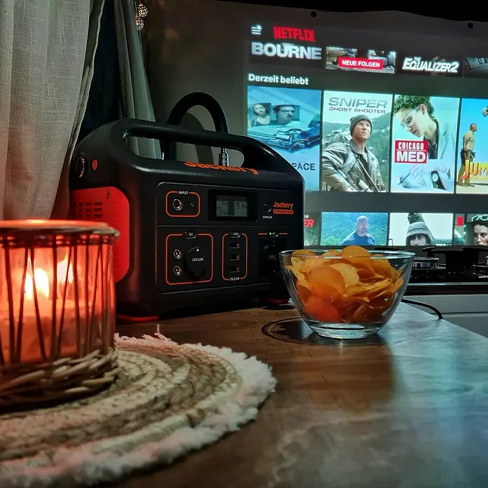 Jackery Estación de energía portátil Explorer 500 Pro EU - 500 Wh, Negro, 24 Ah - Imagen de una central eléctrica Jackery Explorer 500 junto a patatas fritas y una vela, con Netflix al fondo.
