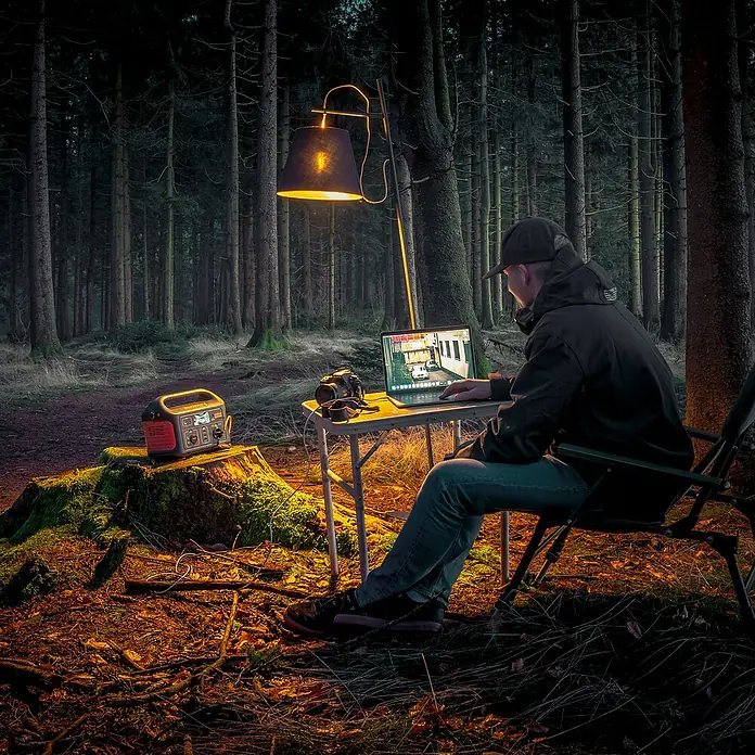 Jackery Estación de energía portátil Explorer 500 Pro EU - 500 Wh, Negro, 24 Ah - Un hombre trabaja en el bosque con un portátil iluminado por una lámpara y una central eléctrica portátil.