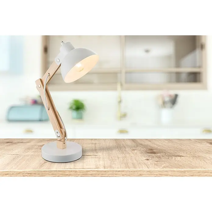 Globo Tischleuchte TONGARIRO - 40 W, L x B x H: 31 x 16 x 42,5 cm, Holz-hell, E27 - Nahaufnahme einer weißen Schreibtischlampe mit Holzdetails, die auf einem Holztisch vor einer verschwommenen Küchenkulisse steht.