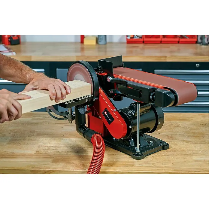 Einhell Lijadora de banda eléctrica de sobremesa TC-US 380 - 380 W, Número de revoluciones de marcha en vacío: 1.500 r.p.m. - Primer plano de una lijadora de banda alisando una pieza de madera, ideal para trabajos de carpintería y proyectos de bricolaje.