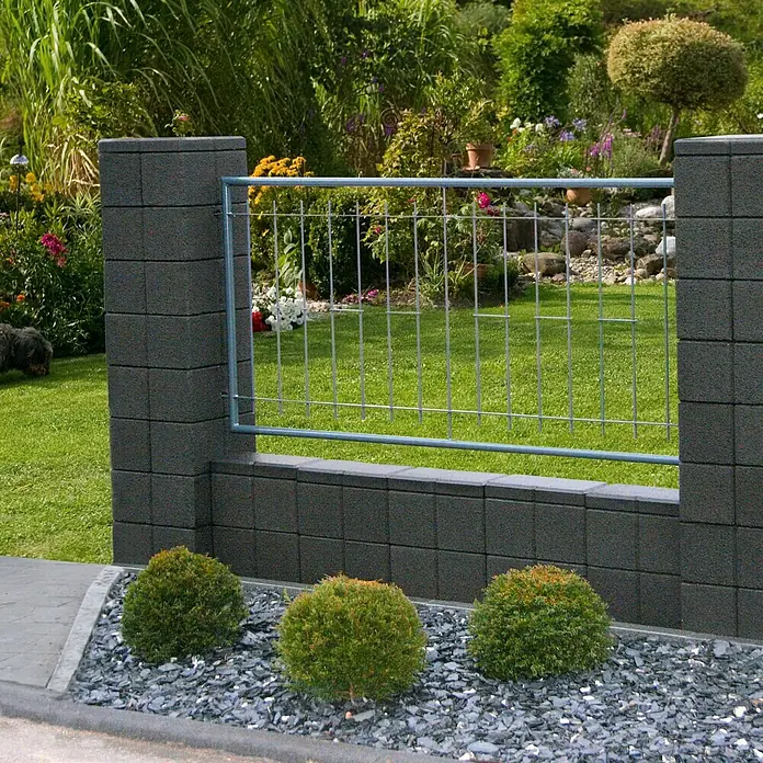 Christoph Gartenmauer Ambienta - 40 x 20 x 20 cm, Anthrazit, Beton - Nahaufnahme eines modernen Zauns mit anthrazitfarbenen Betonsteinen und einem stabilen Metallgitter, umgeben von gepflegten Grünpflanzen und Zierkies.