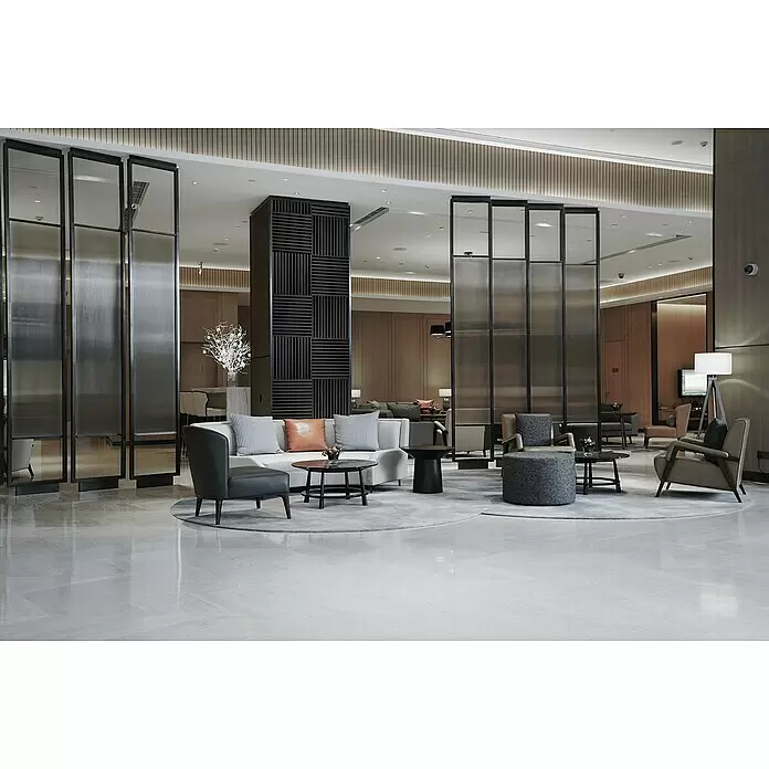 FibroTech Akustikpaneel SQUARE - Black Oak, 520 x 520 x 22 mm - Moderner Hotellobby-Loungebereich mit Sitzgelegenheiten, dekorativen Trennwänden und einer gemusterten Mittelsäule auf hellem Marmorboden.