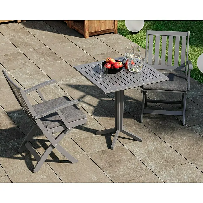 swingcolor Buntlack Kunstharz für Außen - Staubgrau, Seidenmatt, 750 ml, Lösemittelbasiert - Ein graues Gartentischset mit zwei Stühlen auf einer Terrasse, ideal für Mahlzeiten im Freien. Das Set umfasst einen Tisch mit Obstschale und Getränken.