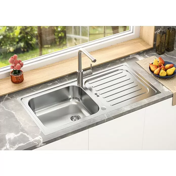 Respekta Einbauspüle Riverside - 100 x 50 cm, Edelstahl - Edelstahl-Küchenspüle mit Abtropffläche und modernem Wasserhahn, installiert in einer grauen Marmor-Arbeitsplatte am Fenster.