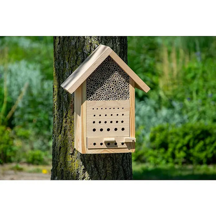 Dobar Bienenhaus Maja - L x B x H: 22,5 x 14 x 29,5 cm, Kiefer - Detailaufnahme eines hölzernen Insektenhotels, das an einem Baum befestigt ist, mit verschiedenen Bohrungen und Röhren für Insekten.